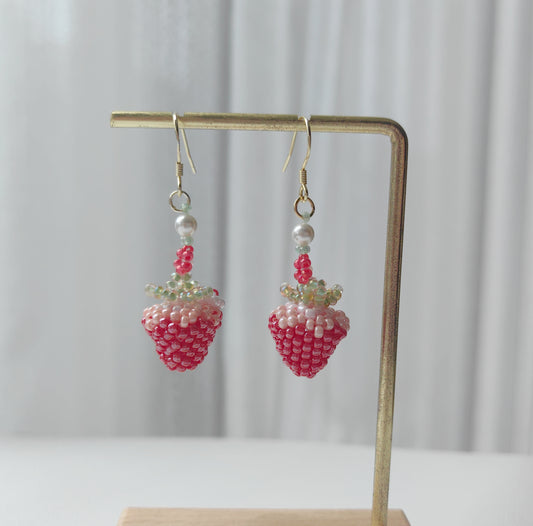 Strawberry-shaped beaded earrings on a stand with a neutral background