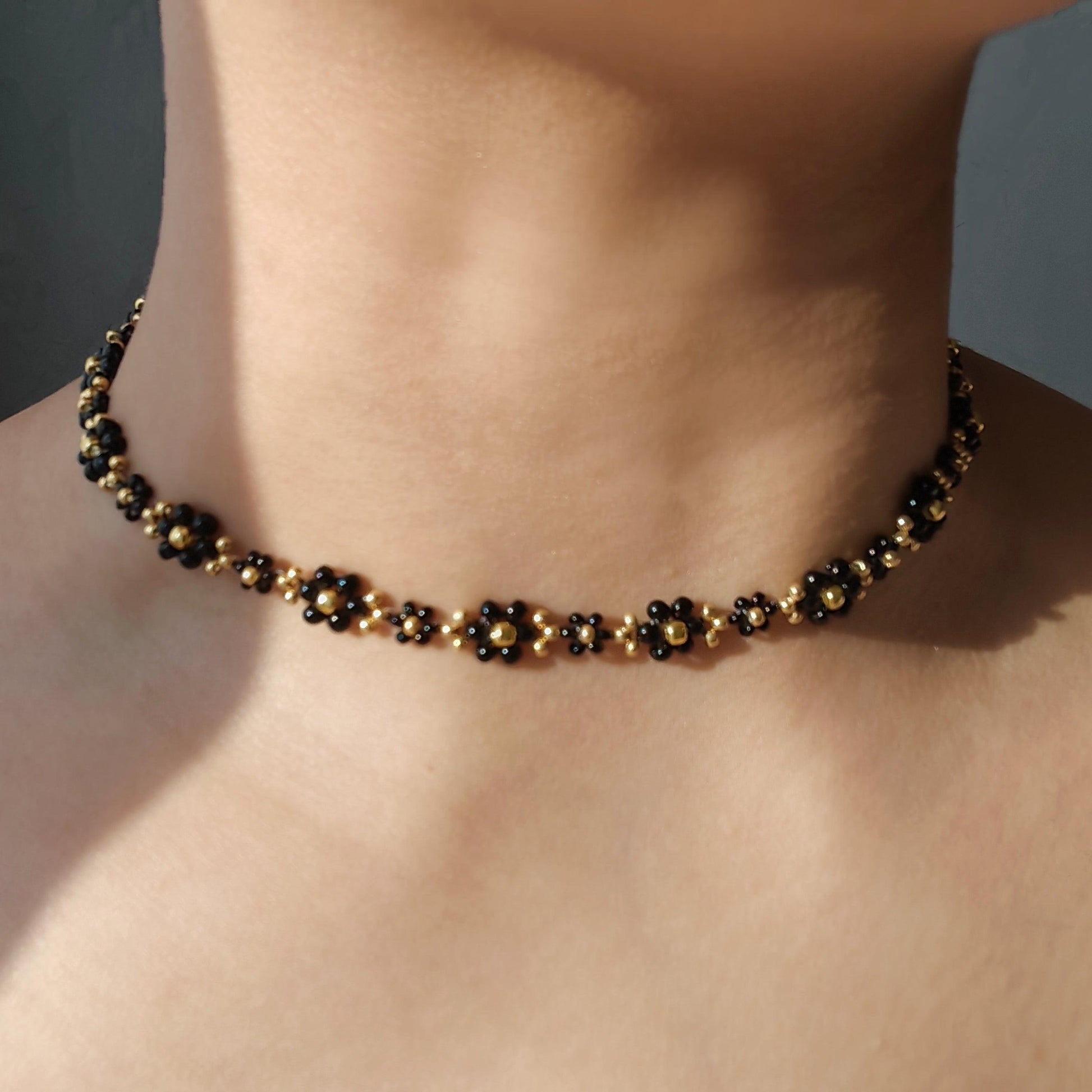 Black daisy beaded necklace worn on neck with black and gold seed beads