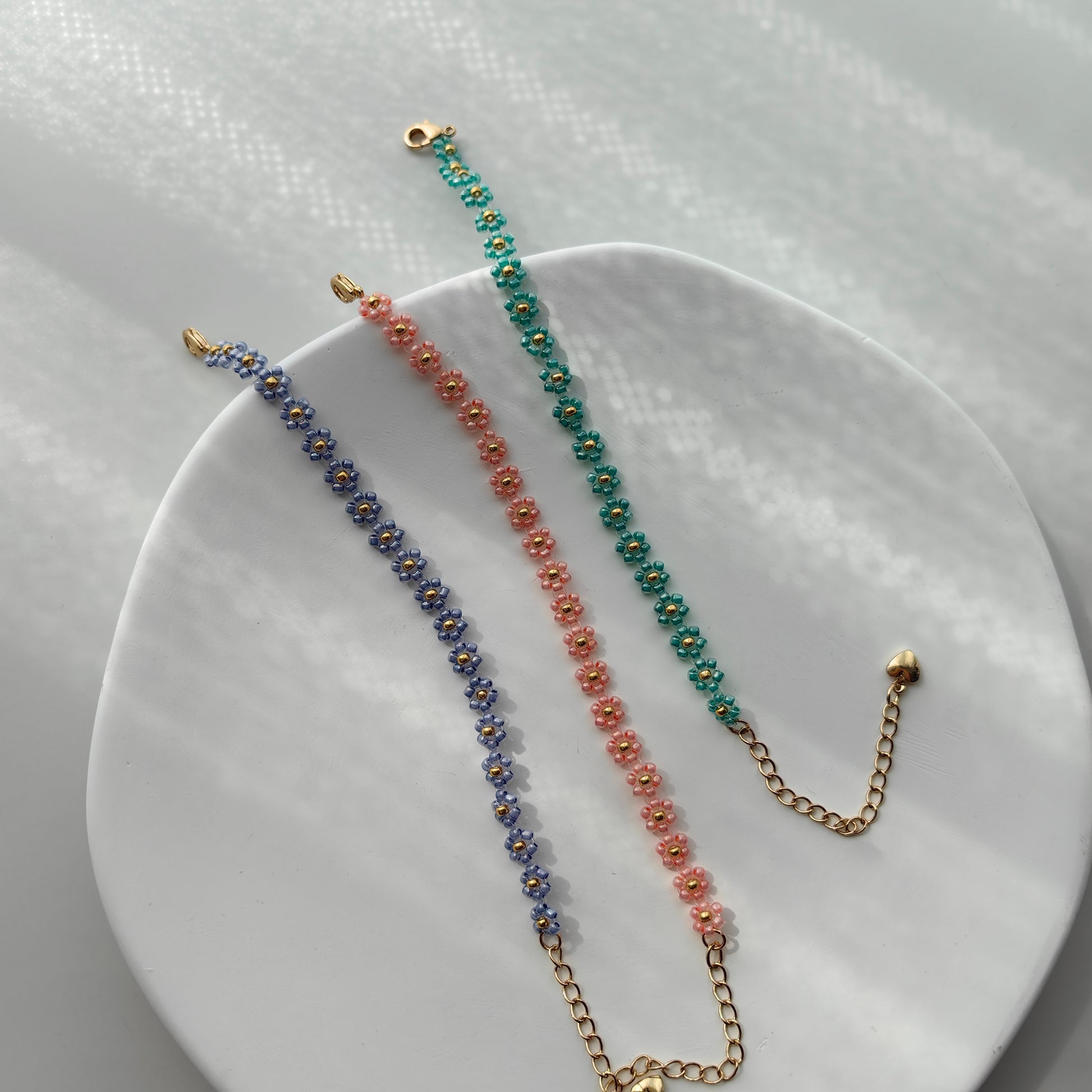 Blue, pink, and green daisy beaded bracelets displayed on white plate, colorful handmade seed bead bracelets