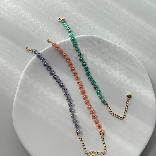 Blue, pink, and green daisy beaded bracelets displayed on white plate, colorful handmade seed bead bracelets