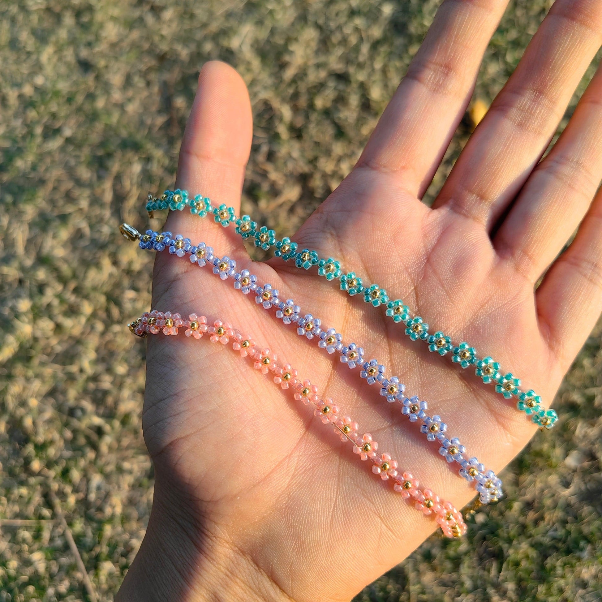 Blue, pink, and green daisy seed bead bracelets worn on hand, delicate handmade floral bracelets
