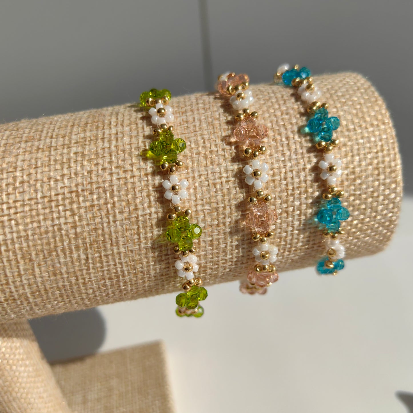 Three Crystal & White Seed Bead Bracelets in pink, blue, and green displayed on bracelet stand