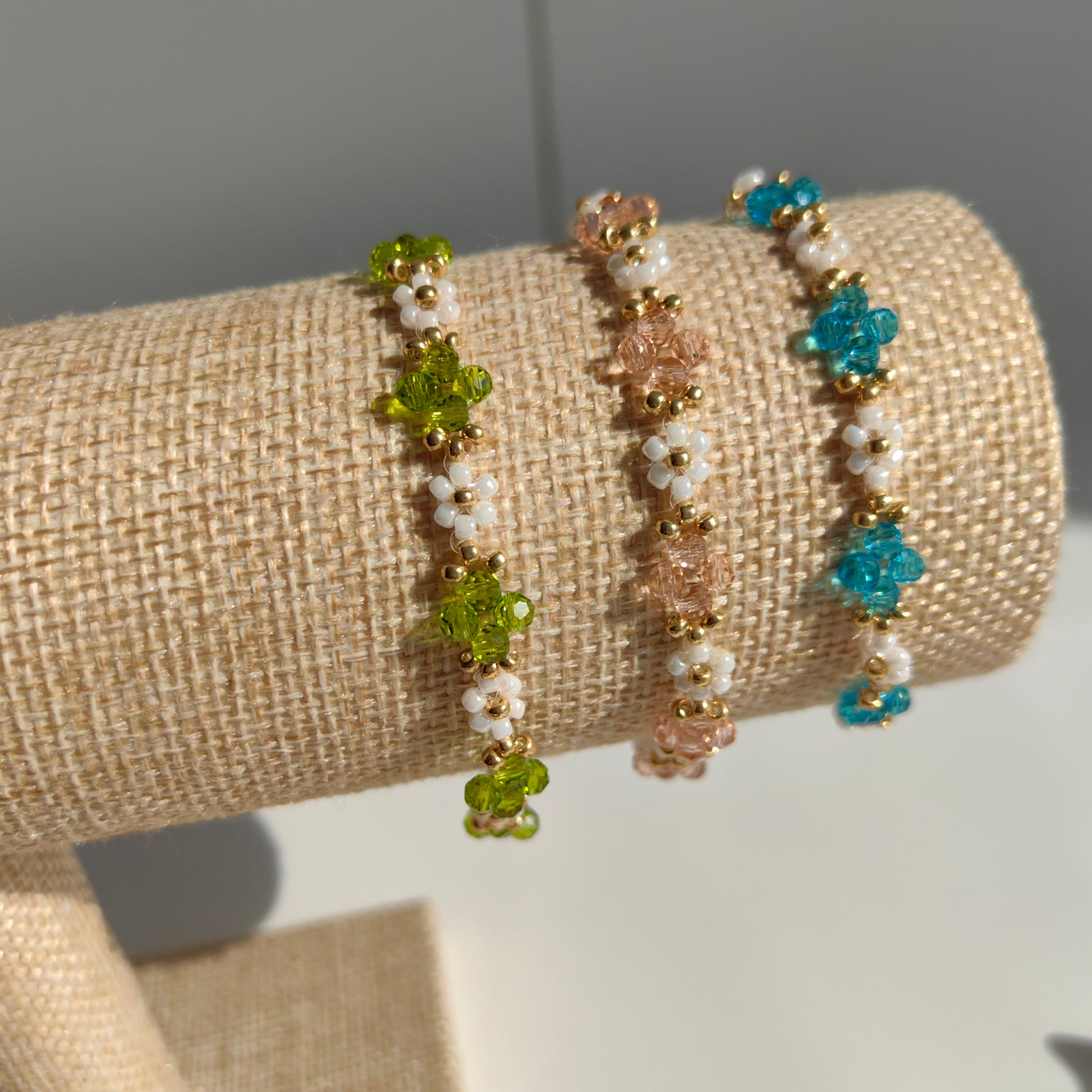 Three Crystal & White Seed Bead Bracelets in pink, blue, and green displayed on bracelet stand