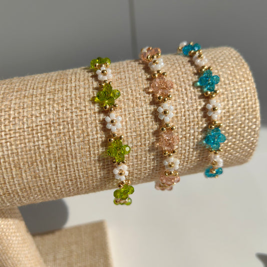 Three Crystal & White Seed Bead Bracelets in pink, blue, and green displayed on bracelet stand