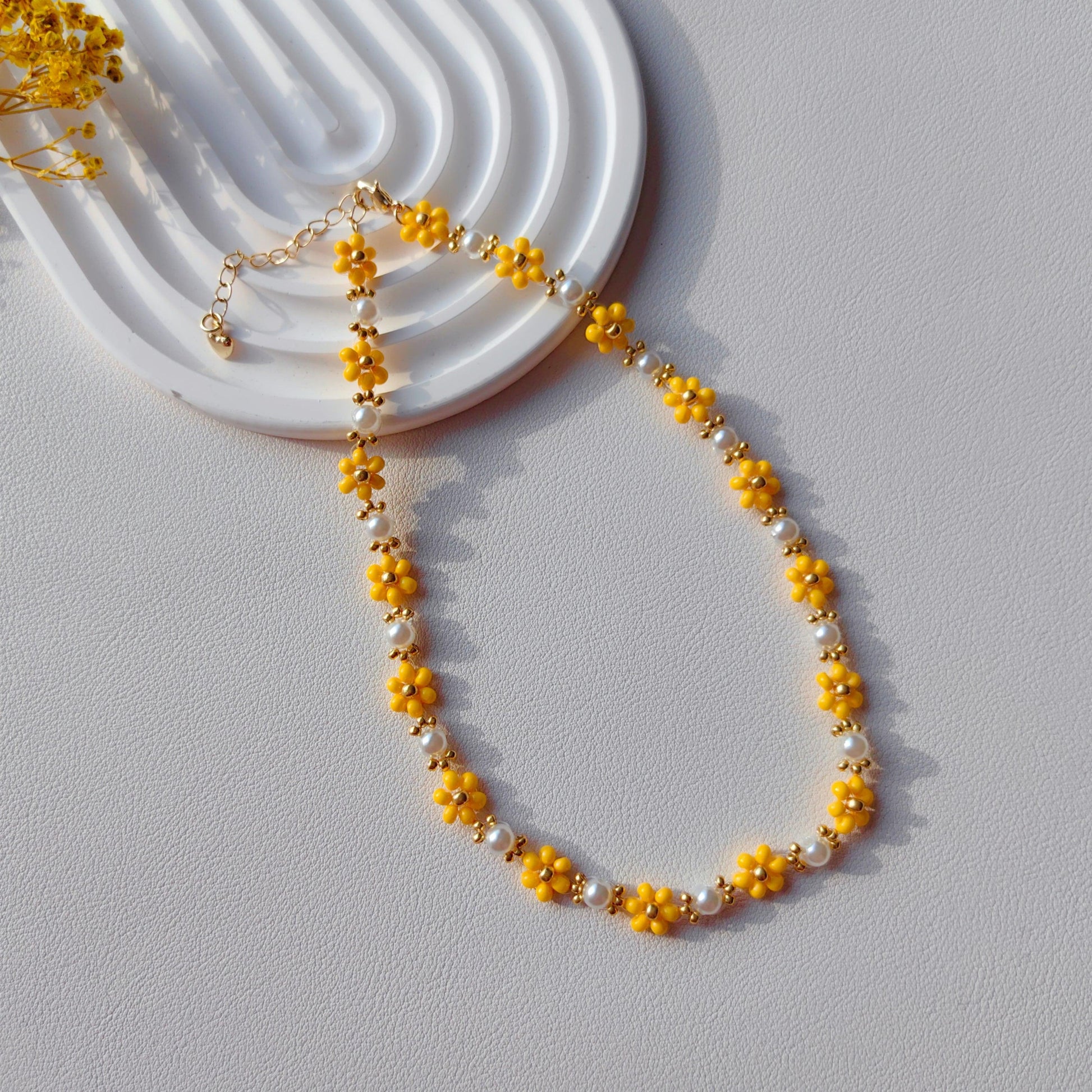 Yellow seed bead and pearl Dandelion necklace displayed on white plate