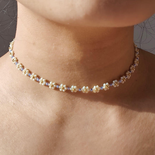 Serene floral beaded necklace worn on neck with white seed bead flowers and blue bead accents