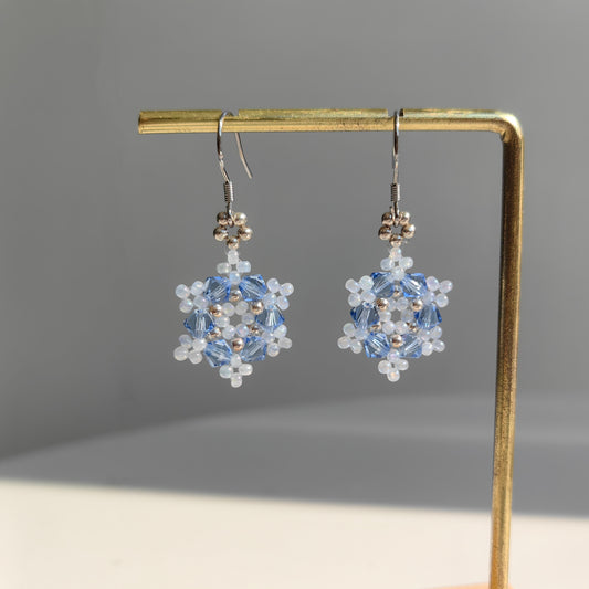 Handmade snowflake bead earrings displayed on an earring stand