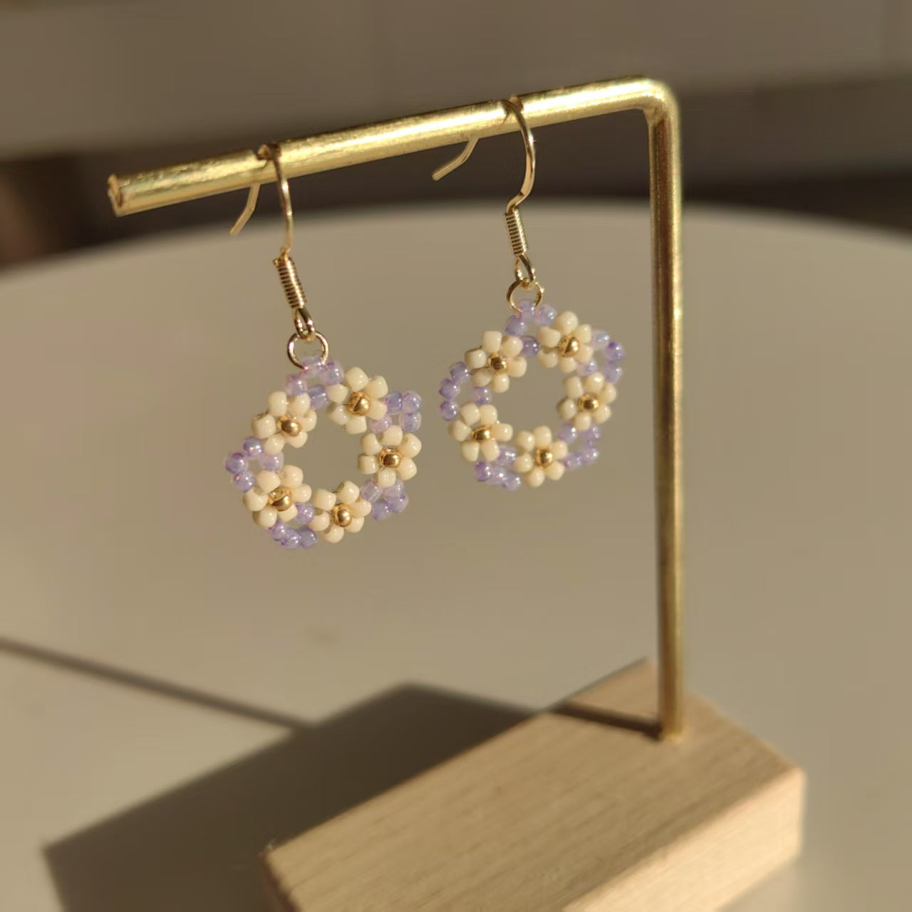 White purple and gold beaded hoop earrings displayed on stand